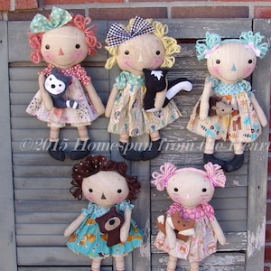 Puede incluir: Seis muñecas de trapo hechas a mano con pelo de lana y ropa de tela. Cada muñeca lleva un animal de peluche, incluyendo un gato, una ardilla, un oso y un zorro. Las muñecas están dispuestas en fila sobre un fondo de madera.
