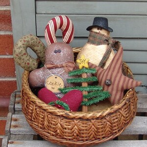 May include: A wicker basket filled with Christmas decorations, including a gingerbread man, a snowman, a star, a candy cane, a small Christmas tree, and two red felt hearts. The gingerbread man has a tag that says "Cookie #4".