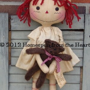 May include: A handmade doll dressed as a nurse, wearing a cream-colored uniform and cap with a red cross. The doll has red yarn hair and is holding a small brown teddy bear with a pink ribbon. The doll is approximately 18 inches tall.