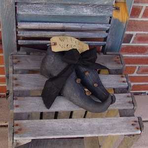 Könnte beinhalten: Ein Paar schwarze Hexenschuhe mit Glöckchen und einer schwarzen Schleife auf einer Holzkiste. Das Etikett lautet "Witchy Woman".
