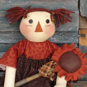 May include: A handmade rag doll with brown hair, a red and brown dress, and a brown felt sunflower.