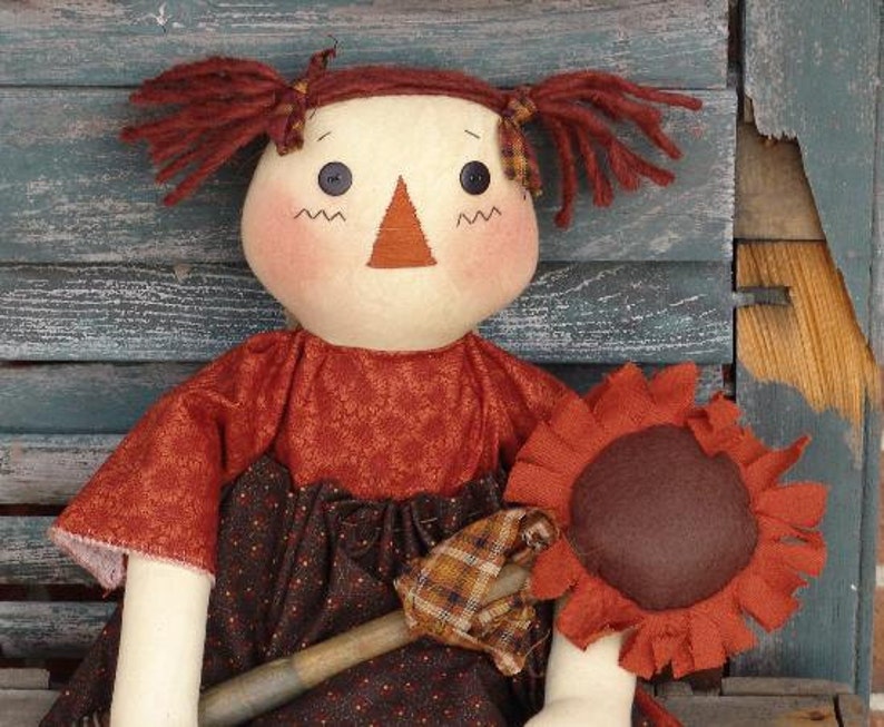 May include: A handmade rag doll with brown hair, a red and brown dress, and a brown felt sunflower.