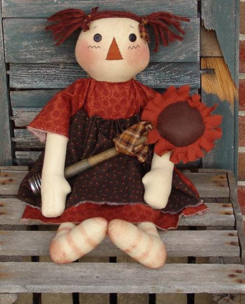 May include: A handmade rag doll with red yarn hair, a brown and white dress, and a brown sunflower in her hand.