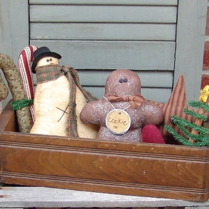 May include: A wooden box filled with handmade Christmas decorations, including a snowman, gingerbread man, candy cane, and a small Christmas tree. The gingerbread man has a tag that says "Cookie Man".