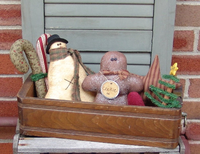 May include: A wooden box filled with handmade Christmas decorations, including a snowman, gingerbread man, candy cane, and a small Christmas tree. The gingerbread man has a tag that says "Cookie Man".