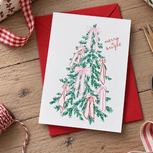 May include: A white greeting card featuring a green line-art illustration of a Christmas tree decorated with pink bows. The text "merry & bright" is printed in red ink on the right side of the card. The card is placed on top of a red envelope.