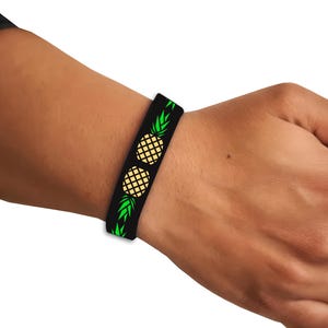 May include: Black silicone bracelet with a repeating pattern of green pineapple leaves and yellow pineapples.