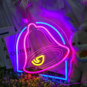 May include: A neon sign shaped like a bell with a pink outline and a blue outline. The bell is lit up with a yellow glow in the center.