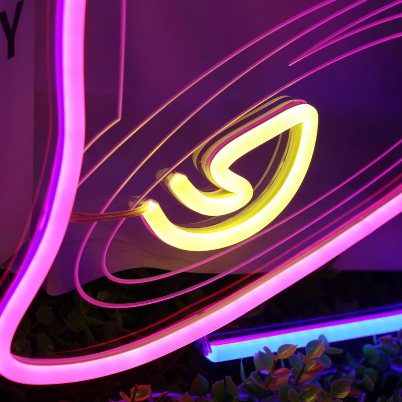May include: A neon sign shaped like a bell with a pink outline and a yellow neon inner shape. The sign is lit up and glowing.