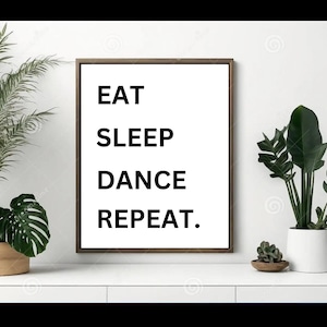 May include: A black and white framed print with the text "EAT SLEEP DANCE REPEAT." The print is hanging on a white wall with a green plant on either side.