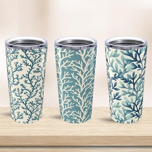 May include: Three stainless steel travel tumblers with lids, each featuring a different blue and white coral reef pattern. The tumblers are cylindrical and sit on a light wood surface.