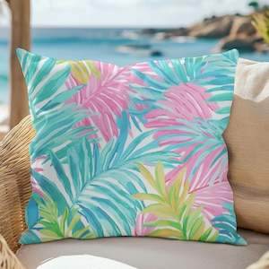 May include: A tropical-themed throw pillow with a white background and a colorful pattern of pink, blue, and green palm leaves.