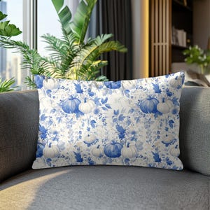 May include: Rectangular decorative pillow with a blue and white pumpkin and floral pattern. The pillow features a repeating design of pumpkins and leaves in shades of blue and white on a cream background. The pillow is resting on a gray sofa.