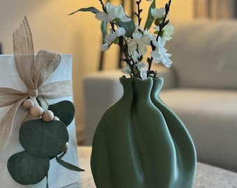 May include: A green ceramic vase with a unique, gathered fabric-like design. The vase is filled with white blossoms.
