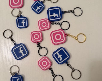 May include: Keychains featuring the Instagram and Facebook logos. The Instagram keychains are pink with white details, while the Facebook keychains are blue with white details. Each keychain has a metal ring for attaching to keys or bags.