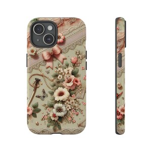 May include: A floral phone case with a delicate lace design and a bow. The case features a variety of pink and white flowers, as well as a touch of green foliage. The background is a soft green colour.