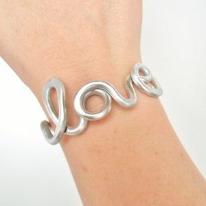 May include: A silver bracelet shaped like the word "love".