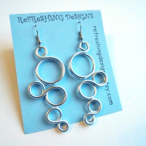 May include: A pair of silver wire earrings featuring a unique, abstract design. The earrings are crafted from multiple loops and circles, creating a contemporary and stylish look.