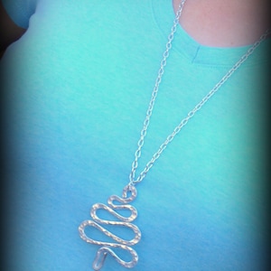 May include: A silver chain necklace with a silver tree-shaped pendant. The pendant is made of twisted wire and has a hammered texture.