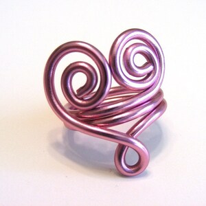 May include: A pink wire ring shaped like a heart with two swirls.