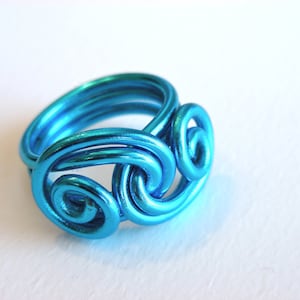 May include: A turquoise blue wire ring with a swirling design. The ring is made of multiple strands of wire that are twisted and intertwined to create a unique and intricate pattern.