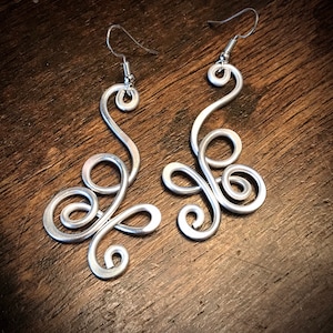 May include: A pair of silver dangle earrings with a swirling, abstract design. The earrings are made of wire and have a simple hook closure.