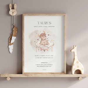 Op de afbeelding: Een ingelijste print met het woord "TAURUS" bovenaan, met een cartoon stier op een wolk. De print bevat affirmaties en wordt tentoongesteld op een houten plank met een giraffenbeeldje en een konijn wanddecoratie.