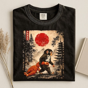 May include: Black t-shirt featuring a graphic of two monkeys in a Japanese-inspired landscape with a red sun and a pagoda. The word "PUNCH" is printed vertically on the left side of the graphic. The shirt has a Comfort Colors tag.