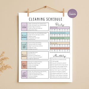 May include: A printable cleaning schedule on a white paper, hanging from a wooden dowel. The schedule is divided into daily and monthly tasks, with checkboxes for each chore. The text is in black, with color-coded sections for different areas of the home.