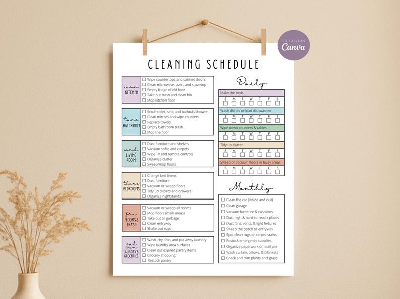 Op de afbeelding: Een afdrukbaar schoonmaakschema op wit papier, hangend aan een houten deuvel. Het schema is verdeeld in dagelijkse en maandelijkse taken, met selectievakjes voor elke klus. De tekst is in zwart, met kleurgecodeerde secties voor verschillende delen van het huis.