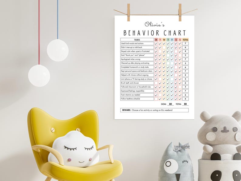May include: A white behavior chart titled "Olivia's Behavior Chart" with a checklist of tasks for each day of the week. The chart is hanging on a wall with a yellow chair and decorative pillows in the foreground.