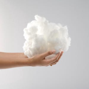 May include: A fluffy, white, cloud-like mass of synthetic fibre fill material. The texture is soft, airy, and voluminous, consisting of fine, interconnected strands that create a rounded, irregular shape held in a cupped position.