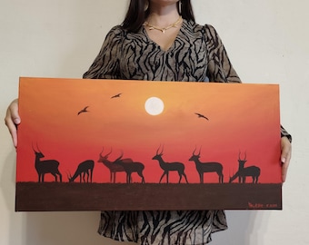 May include: A rectangular canvas painting depicting a savanna landscape at sunset. The scene features black silhouettes of several antelopes standing on dark ground against a vibrant orange and red gradient sky with a white sun and flying birds.