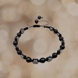 May include: A black and silver beaded bracelet with a sliding knot closure. The bracelet is made with round and hexagonal beads.
