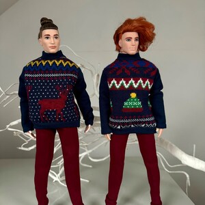 May include: Two dolls wearing festive holiday sweaters with different patterns. One sweater features a reindeer, while the other has a Christmas tree design. Both dolls are wearing maroon pants and white shoes.