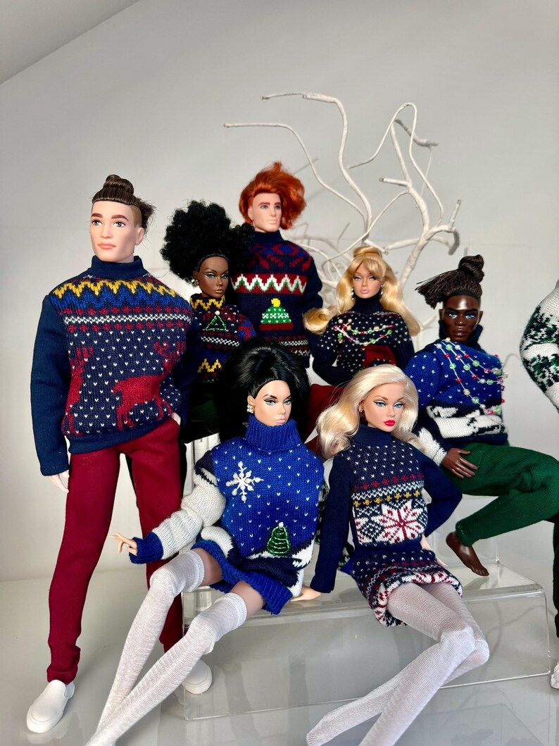 May include: A group of dolls wearing festive holiday sweaters with various patterns, including snowflakes, reindeer, and Christmas trees. The dolls are arranged in a seated and standing position, creating a playful and festive scene.