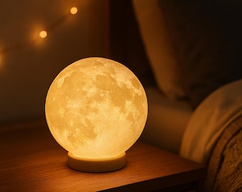 May include: A glowing, spherical moon lamp with a textured surface, resting on a small, round base. The lamp emits a warm, yellow light, creating a cozy ambiance. It sits on a wooden nightstand, suggesting a bedroom setting.