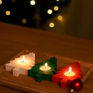 Op de afbeelding: Drie kerstboomvormige kaarshouders in wit, groen en rood, elk met een brandende waxinelichtje. De kaarshouders staan op een houten dienblad, met een rode kerstbal in de buurt. De achtergrond is vervaagd met bokeh-lichten.
