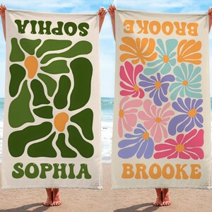 K&ouml;nnte beinhalten: Zwei Strandt&uuml;cher werden gezeigt, jedes mit einem einzigartigen Design. Eines hat ein gr&uuml;nes Blumenmuster mit dem Namen "SOPHIA" in Gr&uuml;n. Das andere Handtuch zeigt bunte Blumen und den Namen "BROOKE" in Orange. Beide Handt&uuml;cher haben einen cremefarbenen Hintergrund.