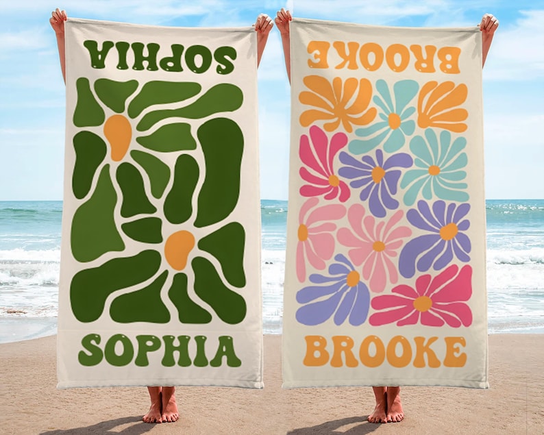 K&ouml;nnte beinhalten: Zwei Strandt&uuml;cher werden gezeigt, jedes mit einem einzigartigen Design. Eines hat ein gr&uuml;nes Blumenmuster mit dem Namen "SOPHIA" in Gr&uuml;n. Das andere Handtuch zeigt bunte Blumen und den Namen "BROOKE" in Orange. Beide Handt&uuml;cher haben einen cremefarbenen Hintergrund.