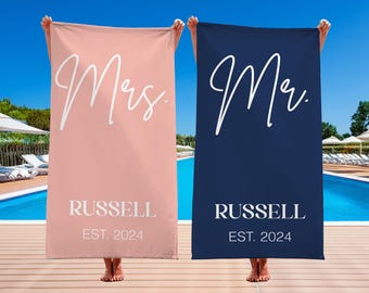 May include: Two beach towels, one pink and one navy blue, with the words "Mrs. RUSSELL EST. 2024" and "Mr. RUSSELL EST. 2024" in white script.