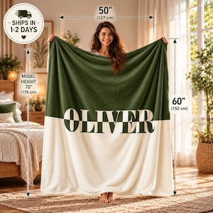 Könnte beinhalten: Eine rechteckige Wohndecke mit zweifarbigem Design, bestehend aus einer dunkelgrünen oberen Hälfte und einer cremefarbenen unteren Hälfte. Der Name OLIVER ist in großen, dunkelgrünen Großbuchstaben mittig aufgedruckt. Die Decke misst 127 cm mal 152 cm.