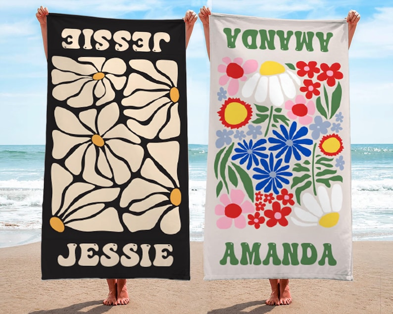 K&ouml;nnte beinhalten: Zwei Strandt&uuml;cher werden gezeigt. Eines ist schwarz mit gro&szlig;en G&auml;nsebl&uuml;mchenmustern und dem Namen "JESSIE" in Wei&szlig;. Das andere ist beige, mit bunten Blumen und dem Namen "AMANDA" in Gr&uuml;n. Beide werden an einem Strand gezeigt.