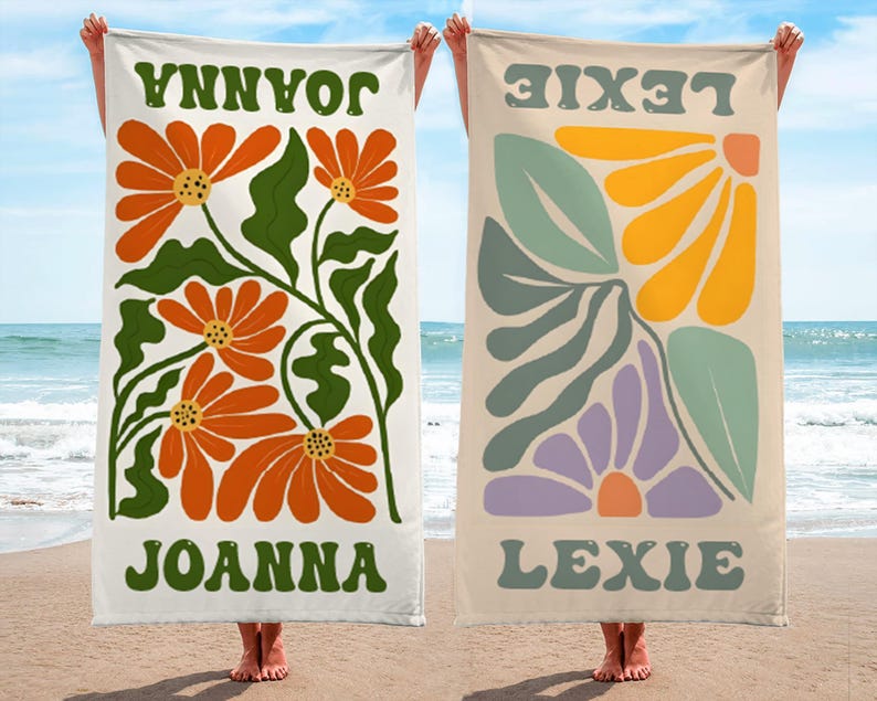 K&ouml;nnte beinhalten: Zwei Strandt&uuml;cher mit Blumendesigns und Namen. Ein Handtuch hat orangefarbene Blumen, gr&uuml;ne Bl&auml;tter und den Namen "JOANNA" in Gr&uuml;n. Das andere hat abstrakte Blumen in Gelb, Lila und Gr&uuml;n mit dem Namen "LEXIE".