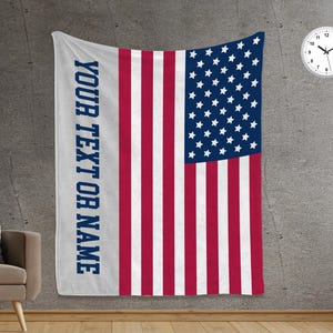 May include: A white throw blanket with a red, white, and blue American flag design. The flag has a blue field of stars and 13 alternating red and white stripes. The text "YOUR TEXT OR NAME" is printed on the left side of the blanket.
