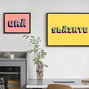 May include: Two framed prints with colourful text. The print on the left has a pink background and says "GR&Aacute;". The print on the right has a yellow background and says "SL&Aacute;INTE".