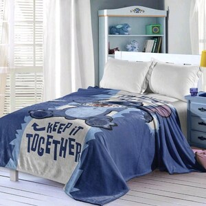 May include: A blue fleece blanket with a cartoon character design. The blanket features the text "KEEP IT TOGETHER" in white and blue. The blanket is draped over a bed with white pillows.