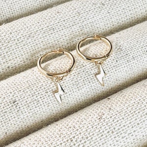 May include: A pair of gold hoop earrings with a small lightning bolt charm hanging from each hoop.