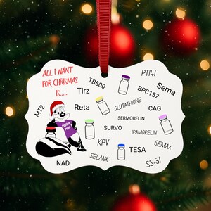 May include: A white Christmas ornament with a red ribbon, featuring a cartoon skunk wearing a purple shirt. The ornament has text that reads "ALL I WANT FOR CHRISMAS IS..." and various scientific terms.