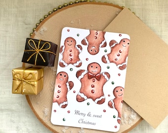 May include: A Christmas card with watercolor gingerbread men and the text "Merry & sweet Christmas." Two small wrapped gifts are on a wooden slice. One gift is gold, and the other is black with a gold bow.